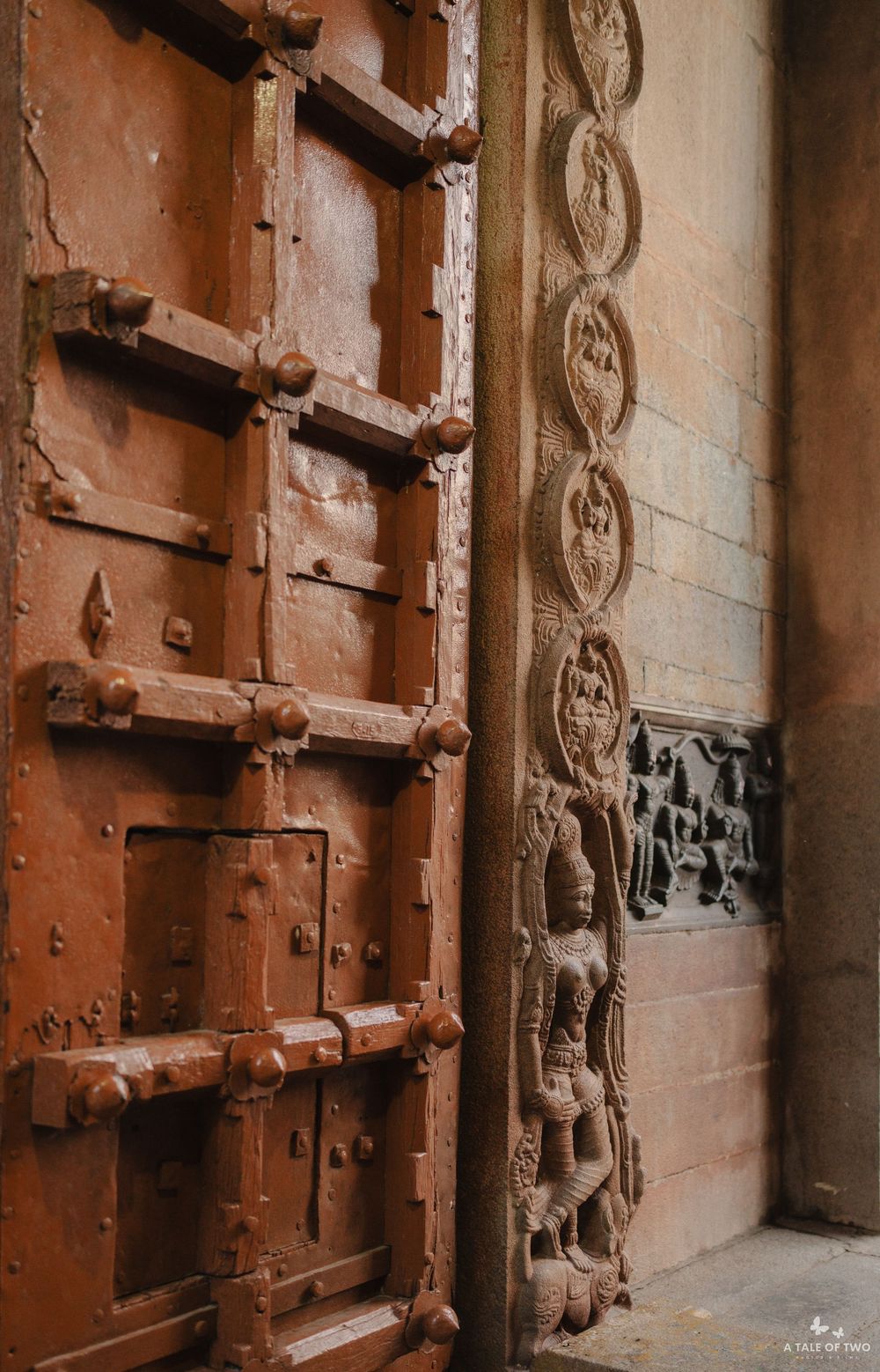 Ancient ornate wooden doors with carved details and metal hardware line a historic stone wall corridor.