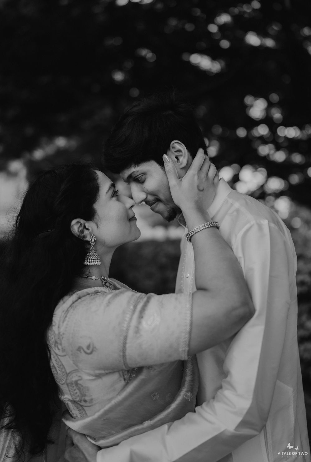 Black and white romantic couple portrait, woman in saree with chandelier earrings, man in kurta, foreheads touching tenderly.