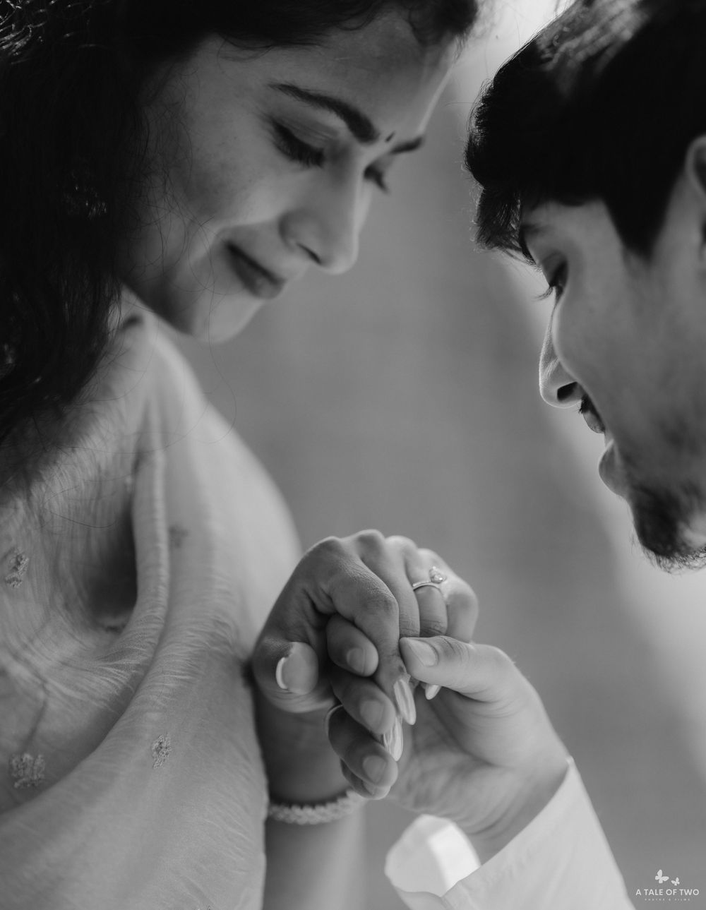 Black and white photo of a couple holding hands tenderly, woman wearing bindi and bangles, romantic portrait.