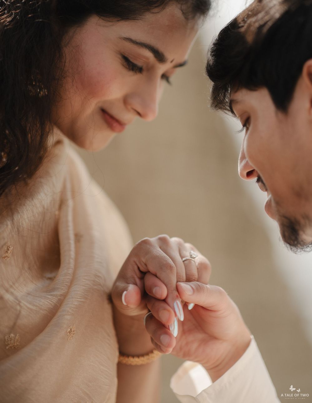 A couple shares an intimate moment as the groom places a ring on the bride's finger during a traditional Indian engagement ceremony.