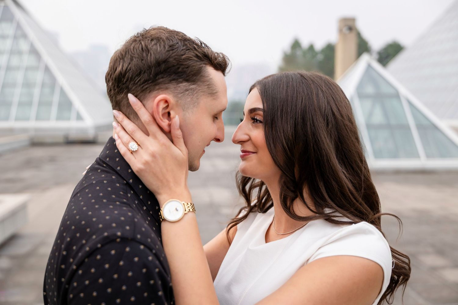 A couple shares romantic moments in front of a modern glass building during a photo session.