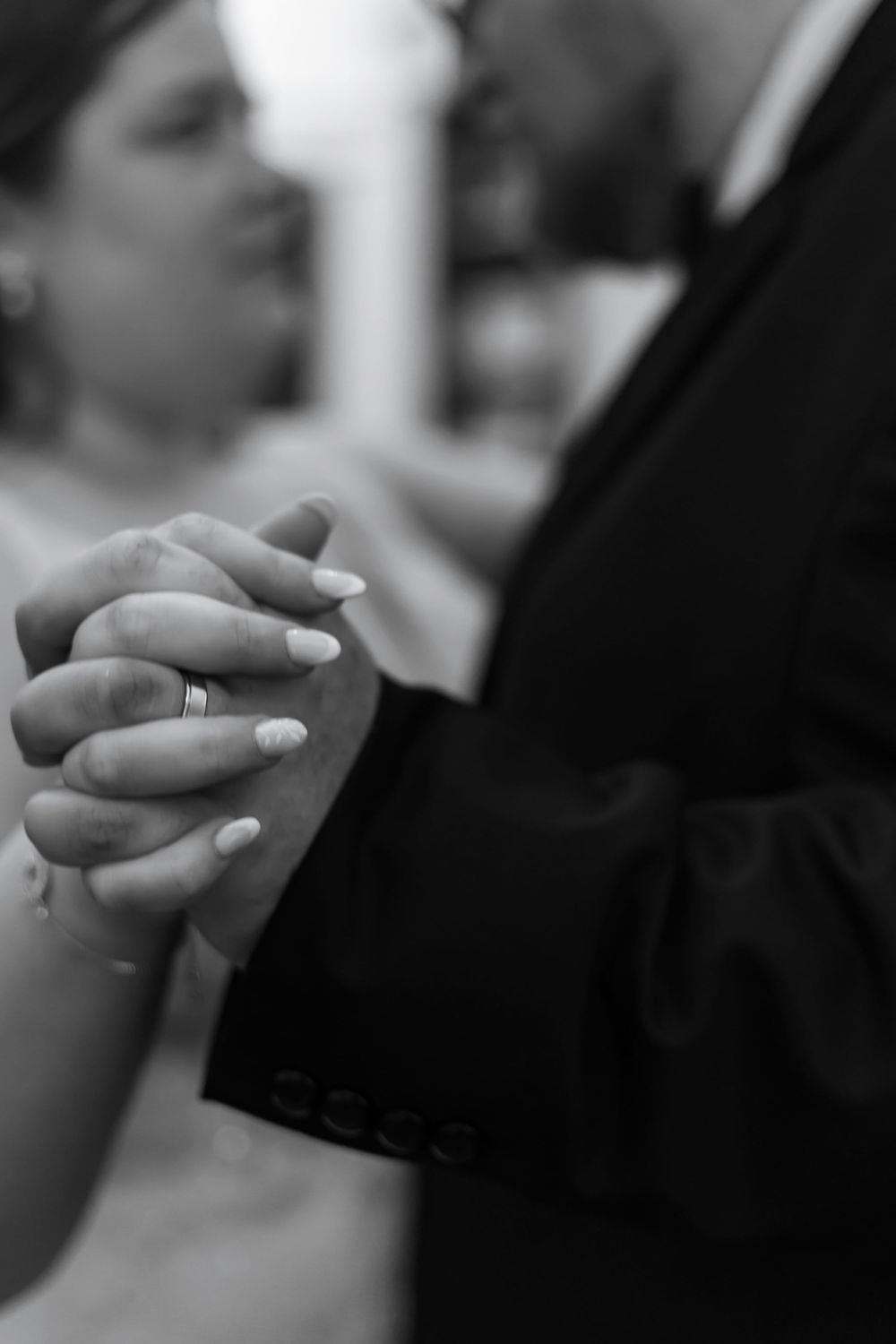 Black and white close-up of hands exchanging wedding rings during ceremony.