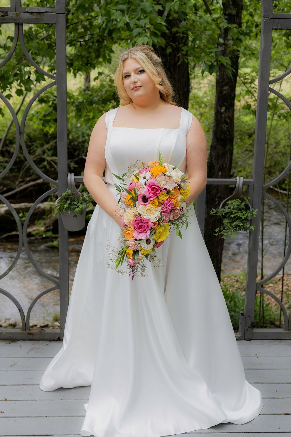 A bride in a white wedding dress poses with a vibrant pink and orange bouquet on a wooden deck.