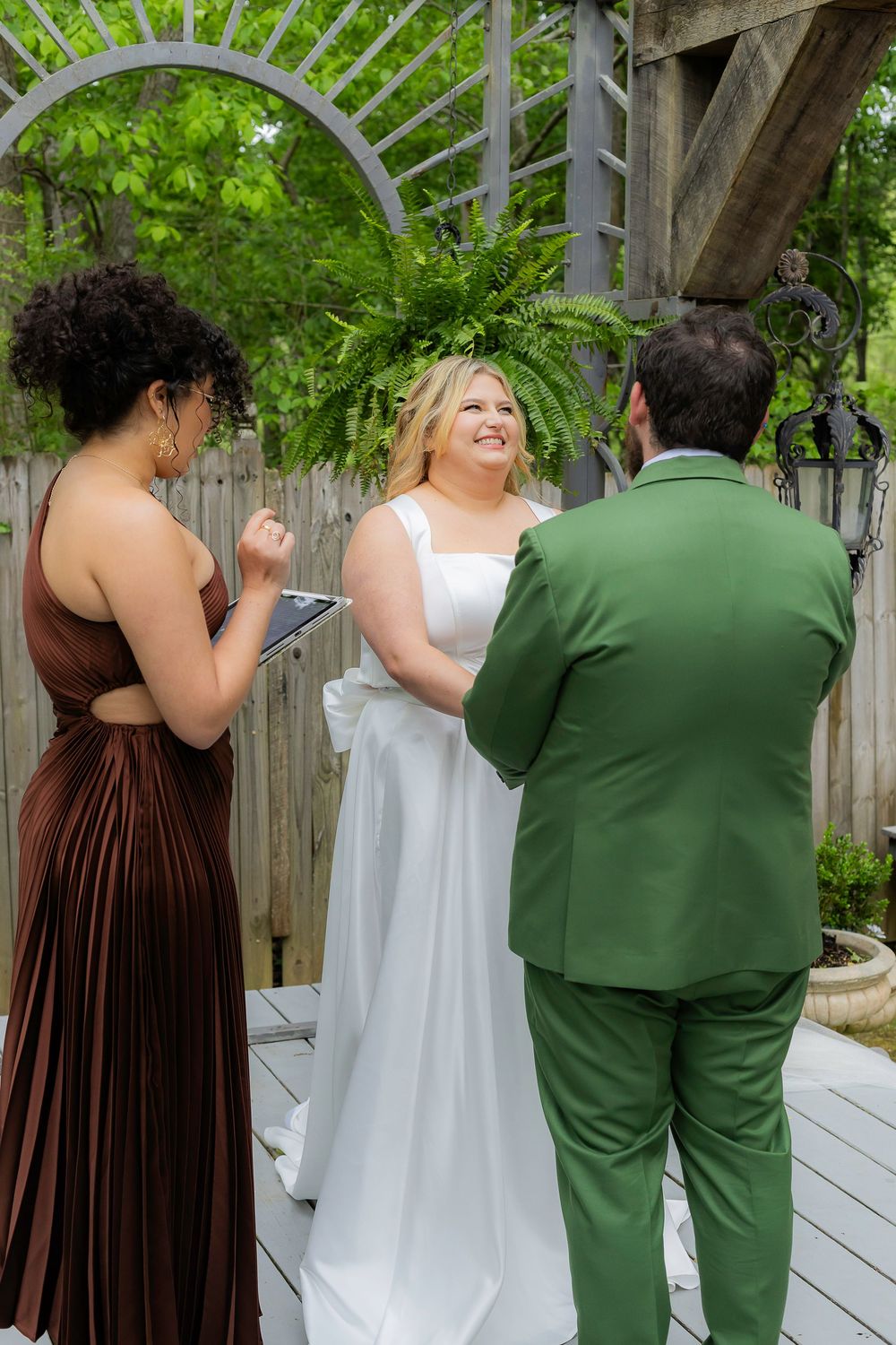 Wedding party members in brown and green attire dance together on an outdoor wooden deck.