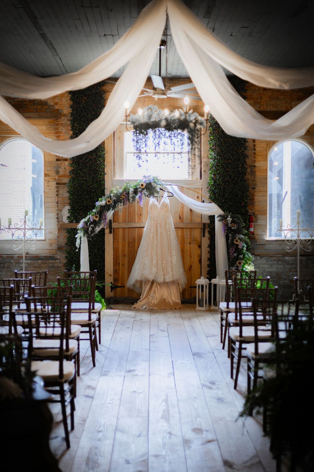 Elegant wedding ceremony setup with draped fabric, floral arch and wooden chairs in a rustic venue.