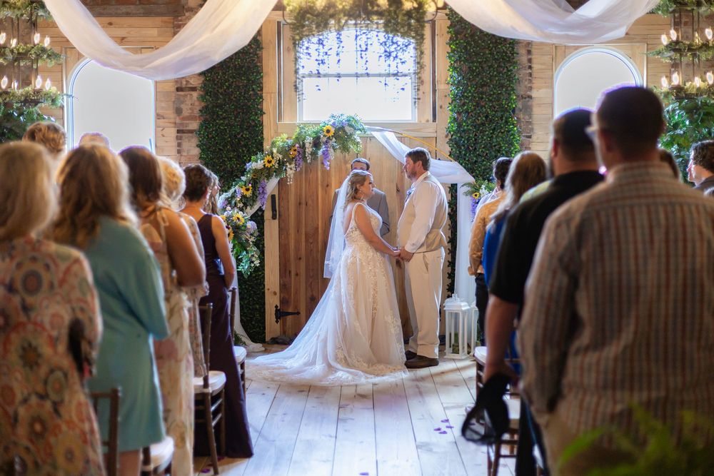 Wedding ceremony in progress with guests watching couple at decorated altar in rustic venue.