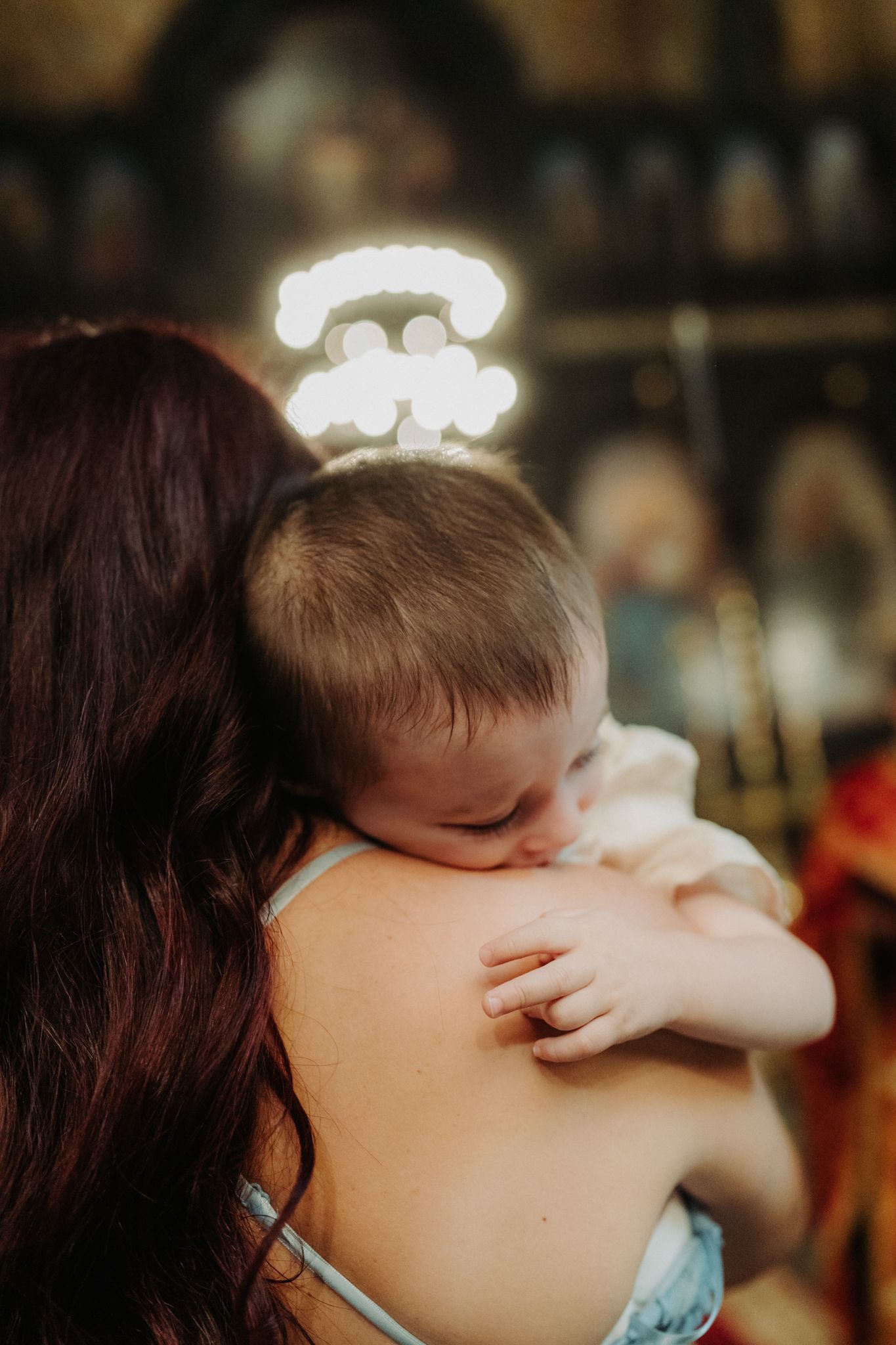 A tender moment captured as a small child wearing a glowing halo headband rests their head on a shoulder in warm lighting.
