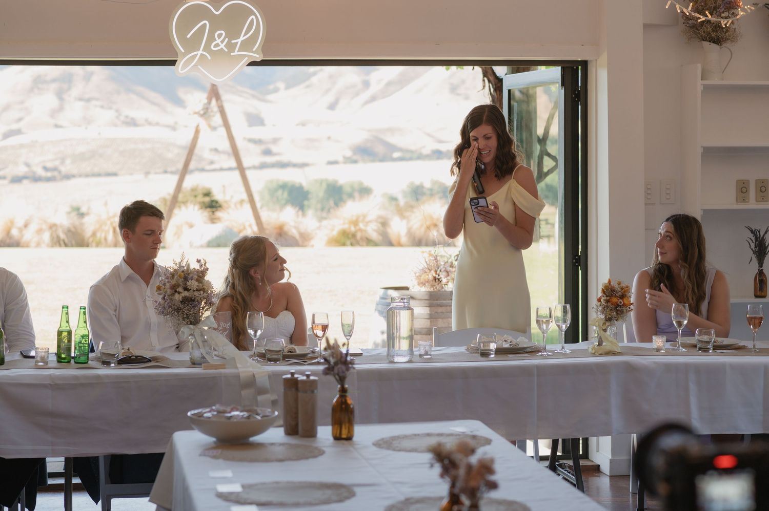 Wedding guests enjoy an elegant reception dinner at long tables with mountain views through large windows.