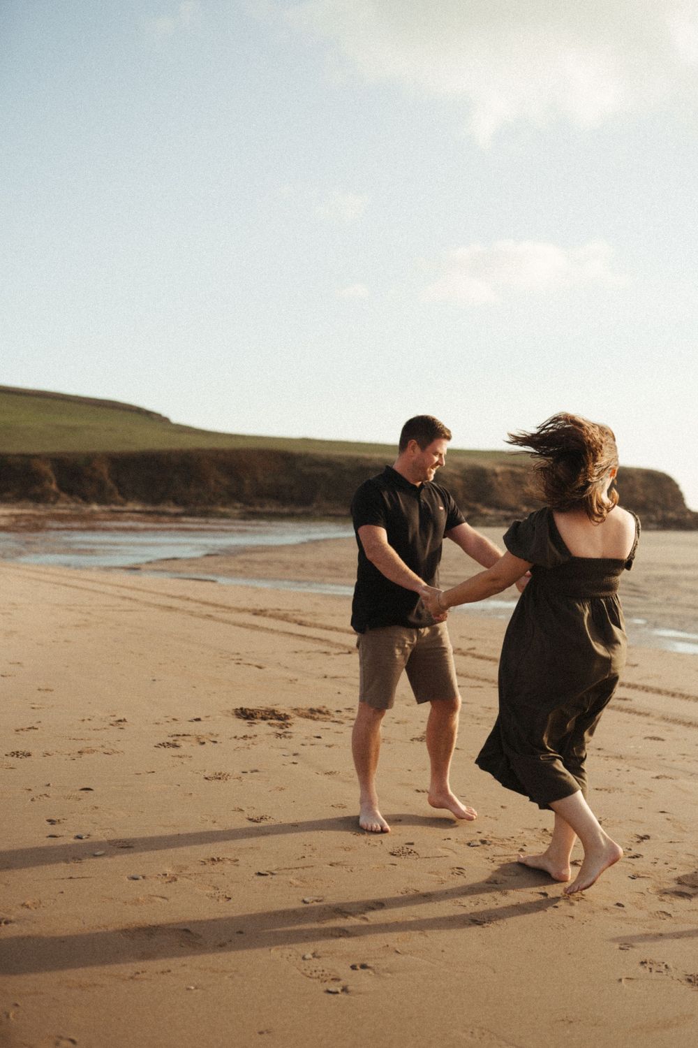 Couple playfully dancing and spinning together on a scenic beach at sunset.