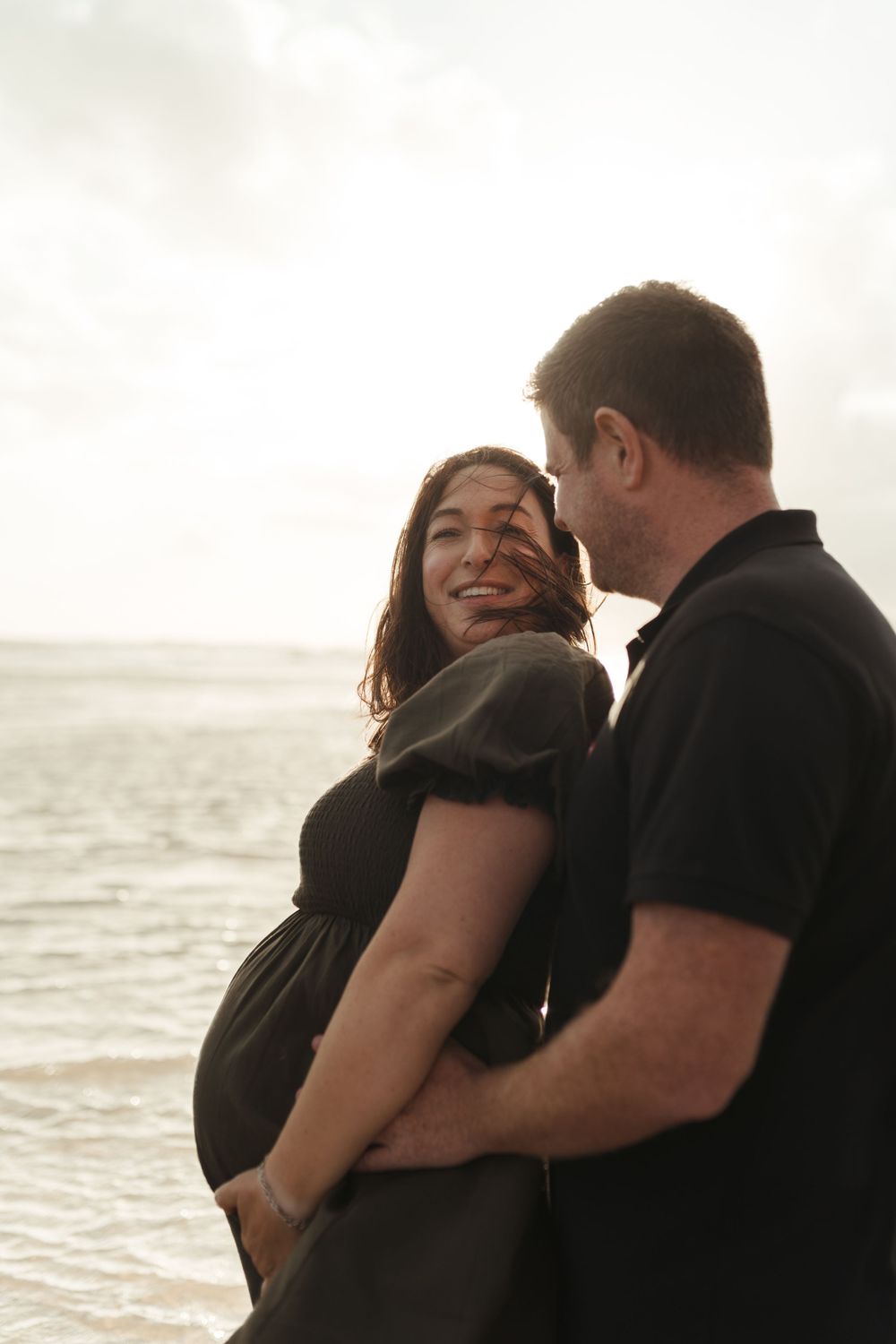 A romantic couple embraces on the beach at sunset in a series of intimate black and white photos.