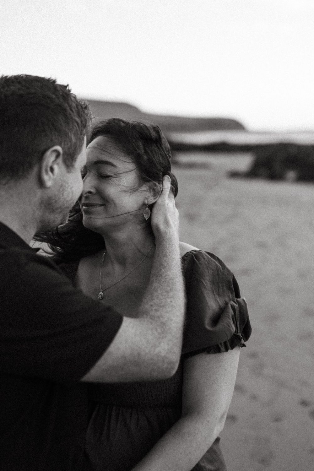 A romantic black and white photo series shows a couple sharing intimate kisses on a beach at sunset.