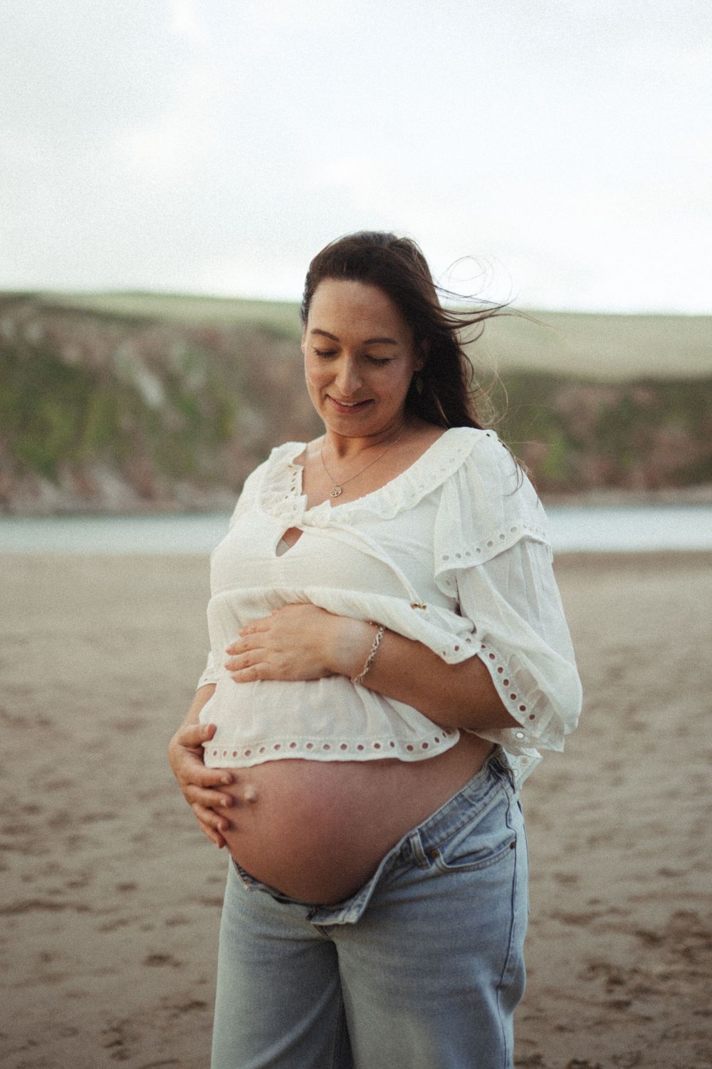 A series of maternity photos showing a pregnant woman in a white top cradling her belly on a beach.