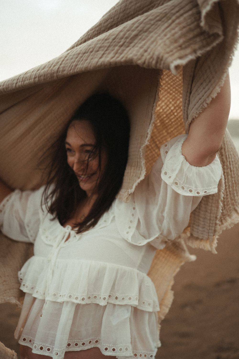 A white lace dress flows in the breeze against a soft brown background.