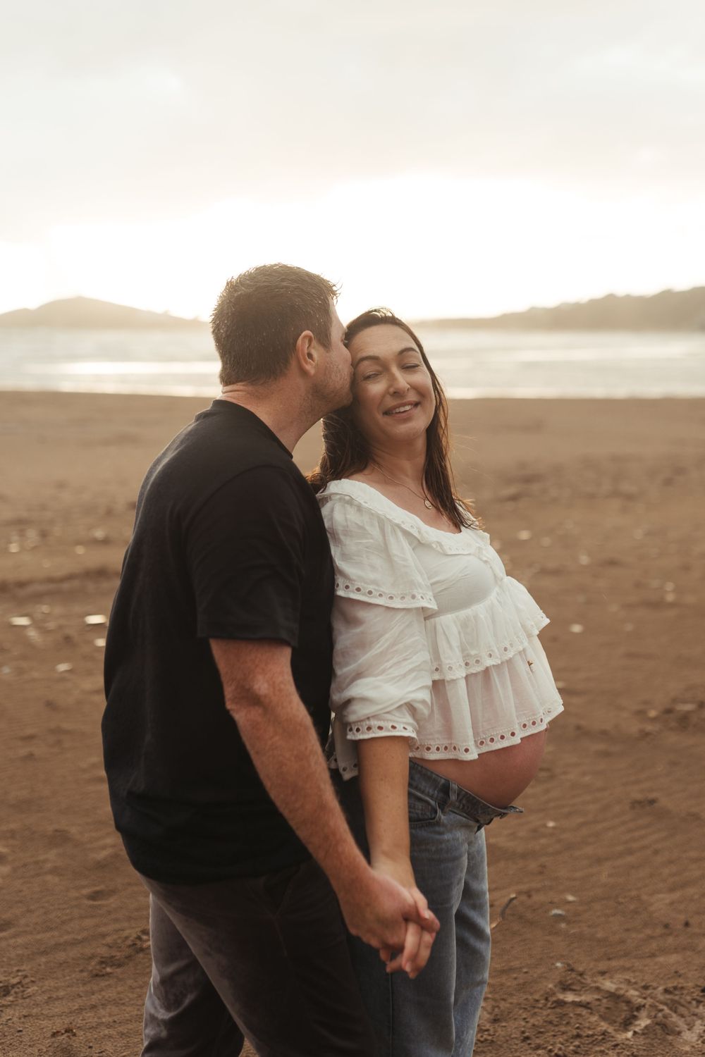 Intimate couple sharing a tender moment on a sandy beach during golden hour.