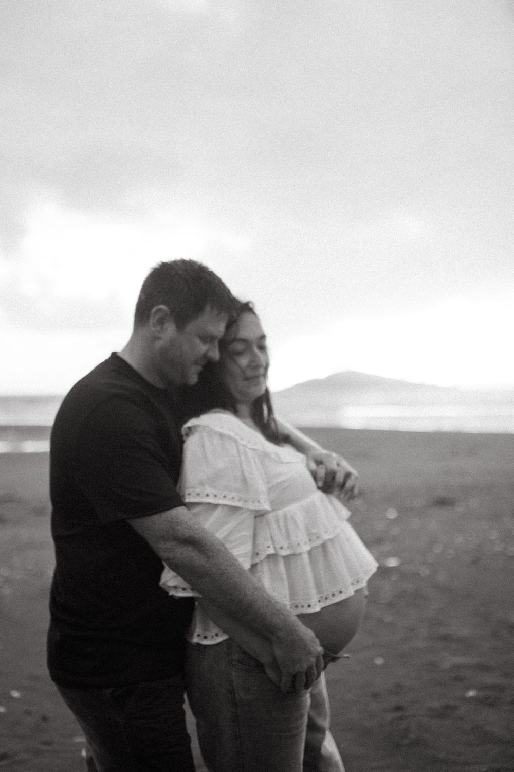A tender moment between a couple in black and white as they embrace on a misty beach.