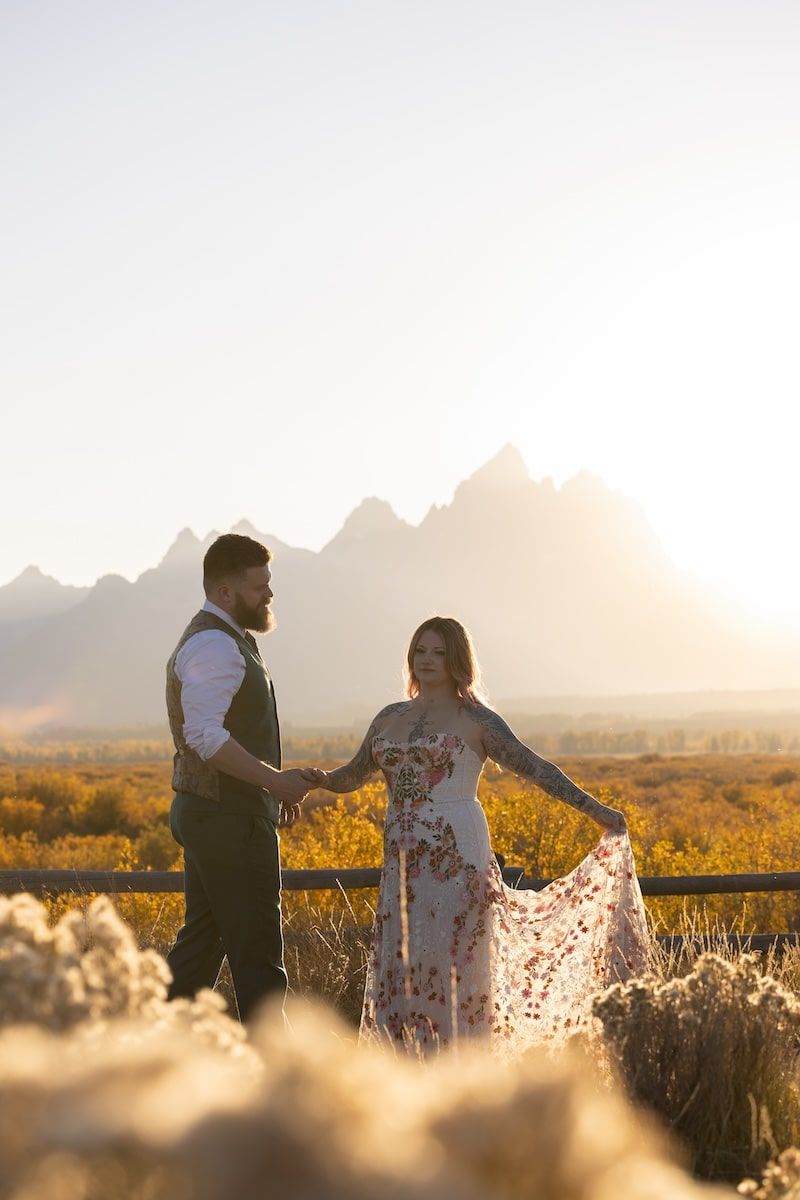 A couple dances together in a golden field at sunset with mountains in the background.
