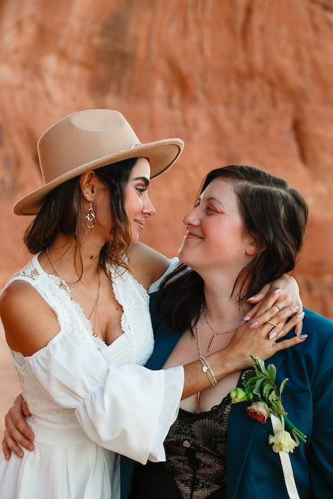 A romantic couple in western wedding attire embrace against a red rock canyon backdrop.