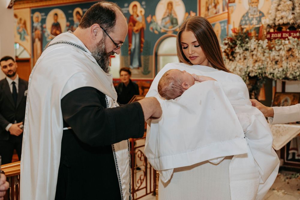 A baby's baptism ceremony takes place in an ornate Orthodox church with religious icons visible in the background.