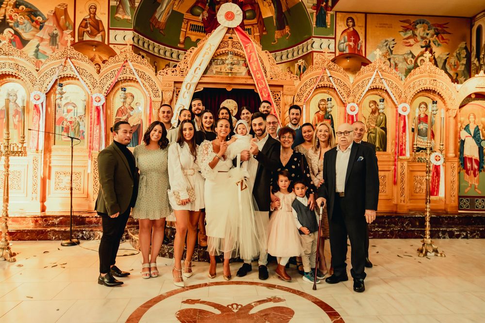 A group of people stand together in front of an ornate gold and red Orthodox church iconostasis during a celebration.