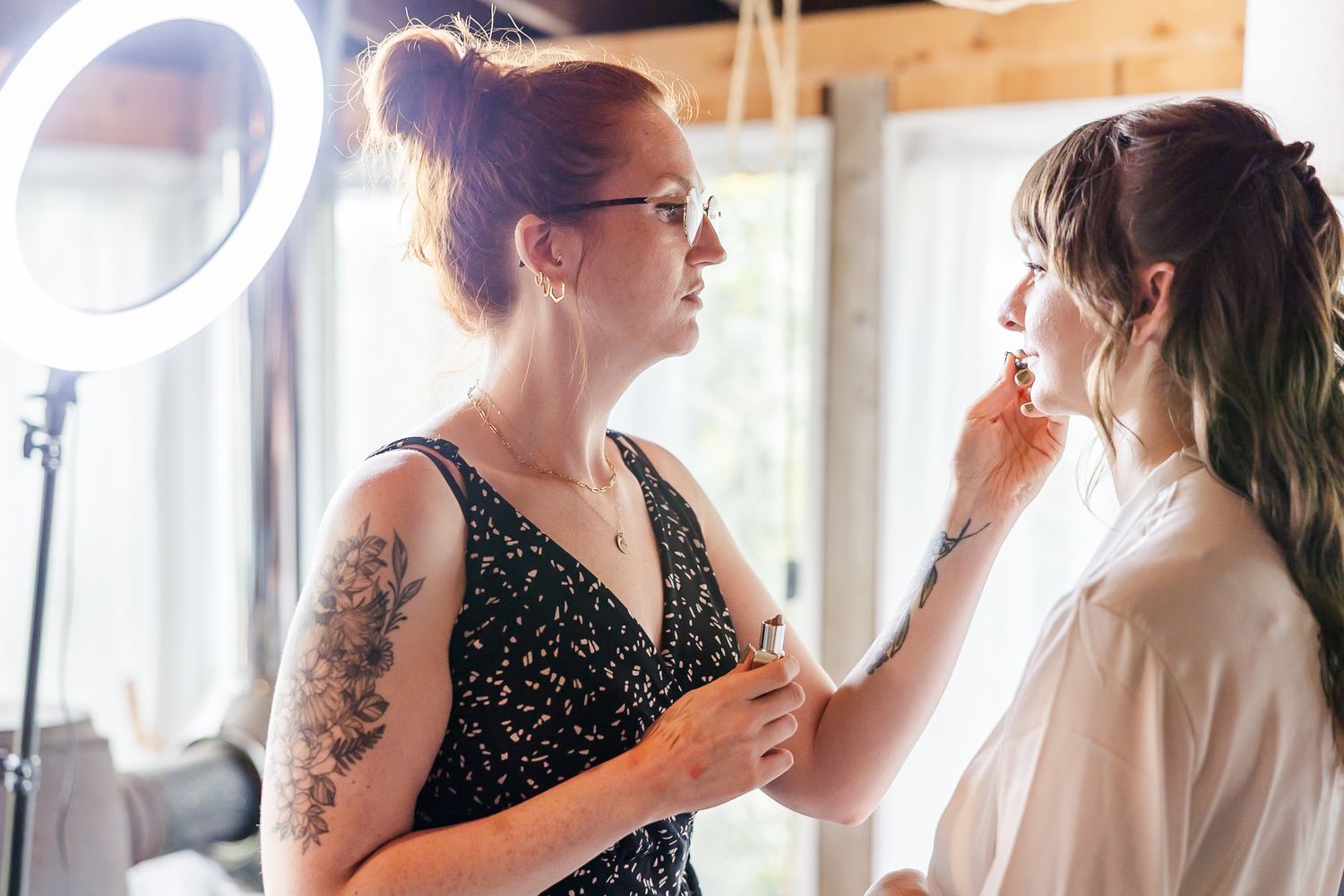 Bridesmaids in black polka dot dresses help with wedding preparations in a bright sunlit room.