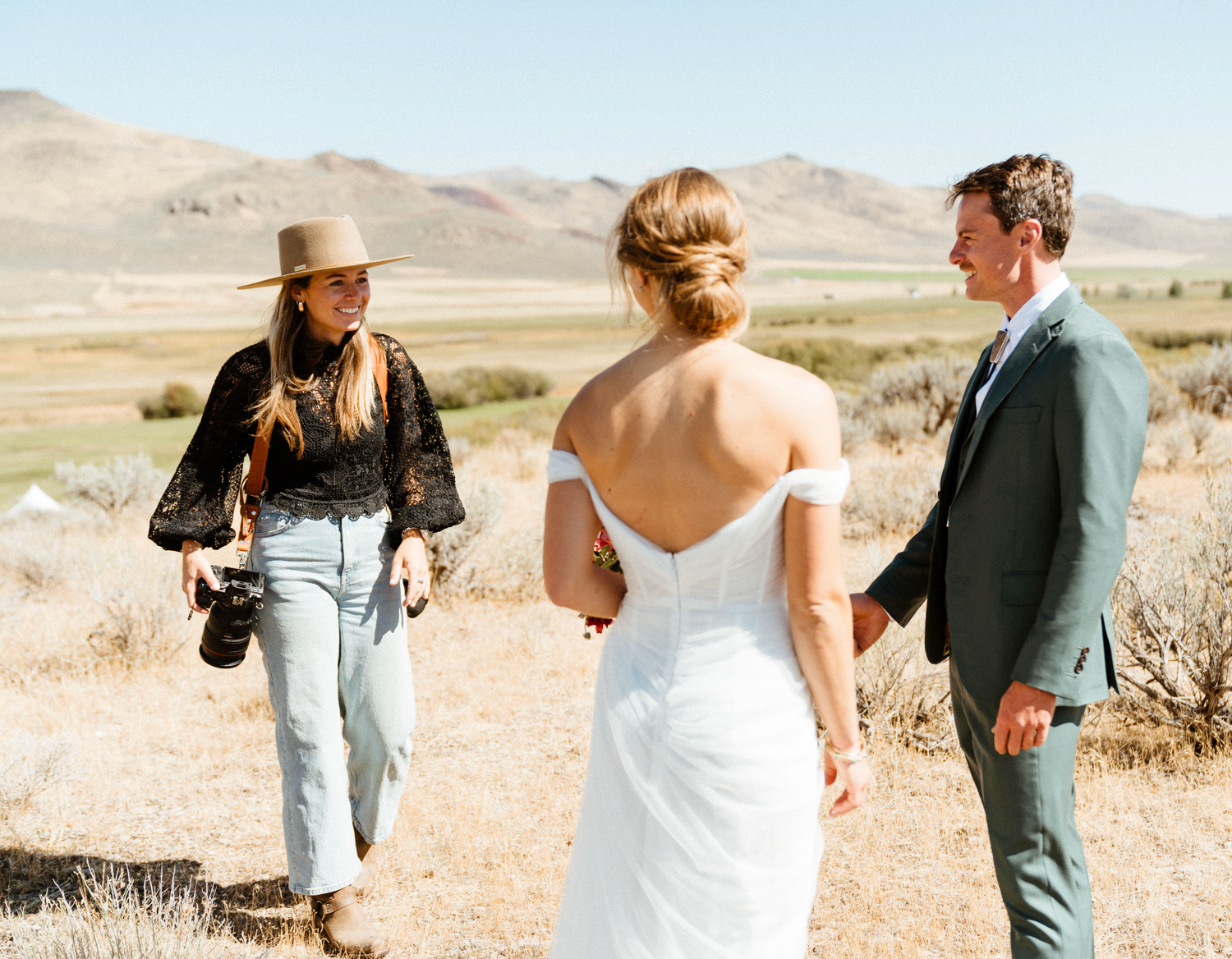 A couple shares intimate moments in a desert landscape with golden grass and mountains in the background.