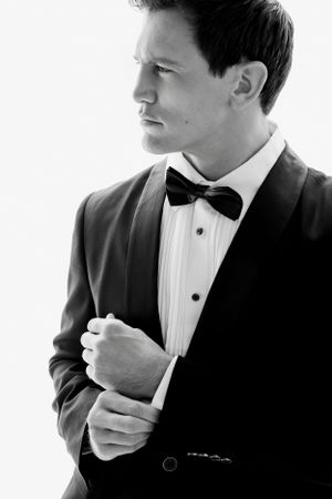 Black and white portrait of a groom adjusting his sleeve in a classic tuxedo with bow tie.