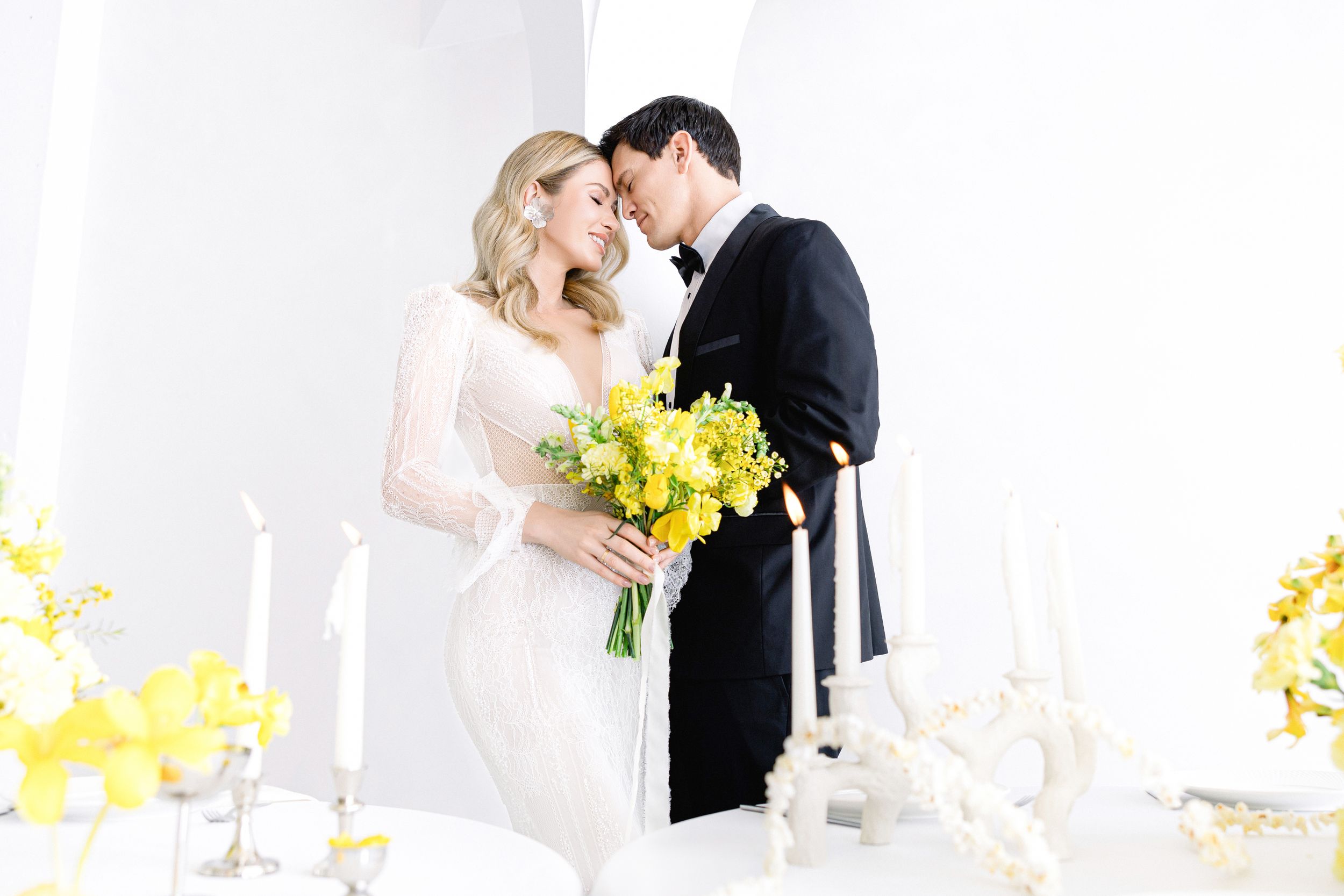 Romantic wedding couple share intimate moment at elegantly decorated reception table with yellow flowers.