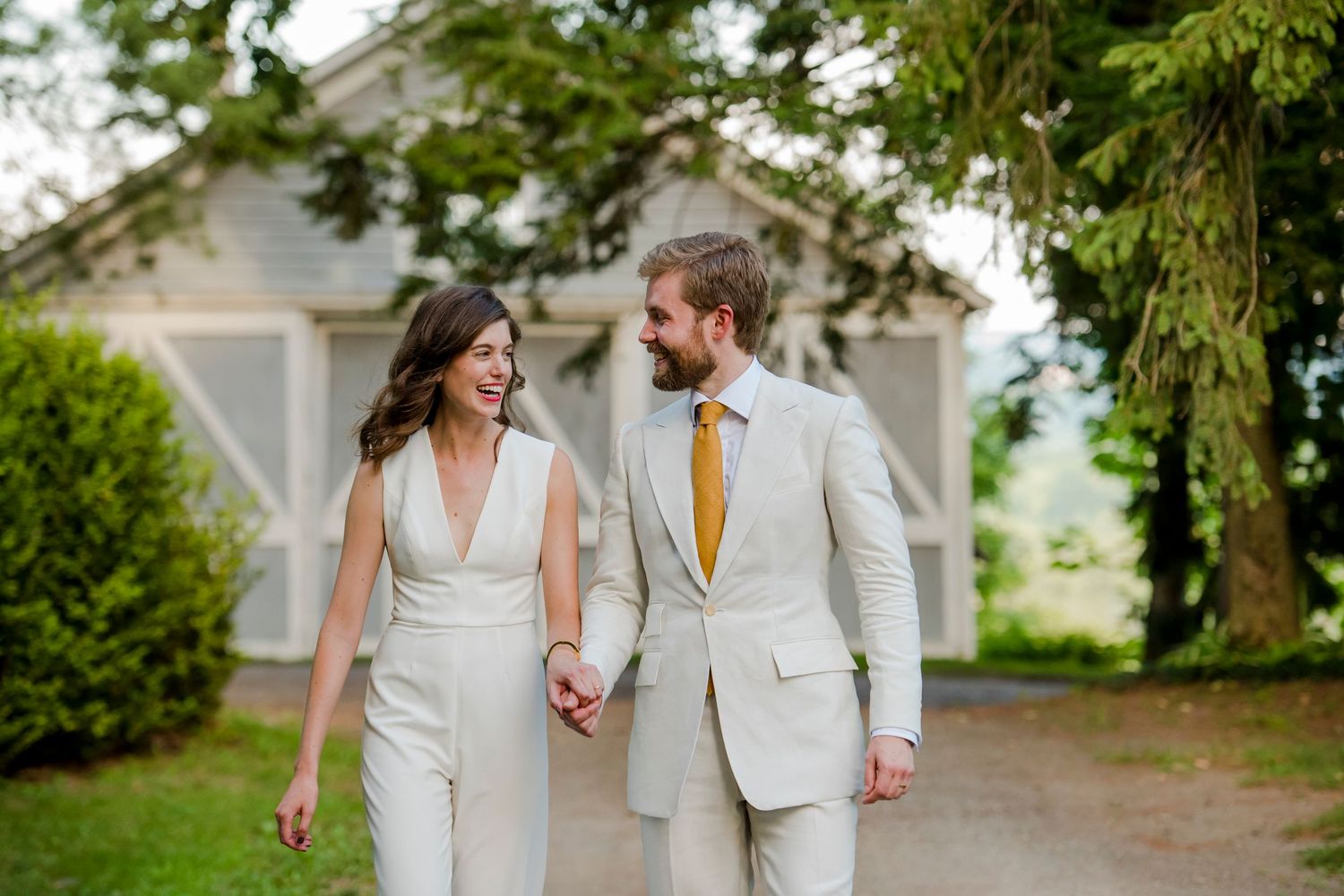 Couple in matching white outfits walking together near a garden gazebo.