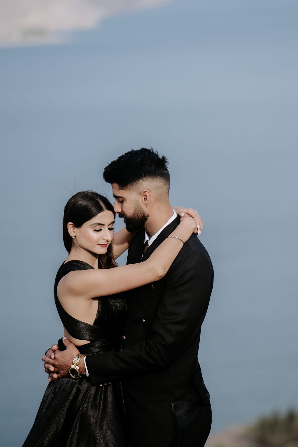 A couple in formal attire share an intimate dance pose against a cloudy sky backdrop.