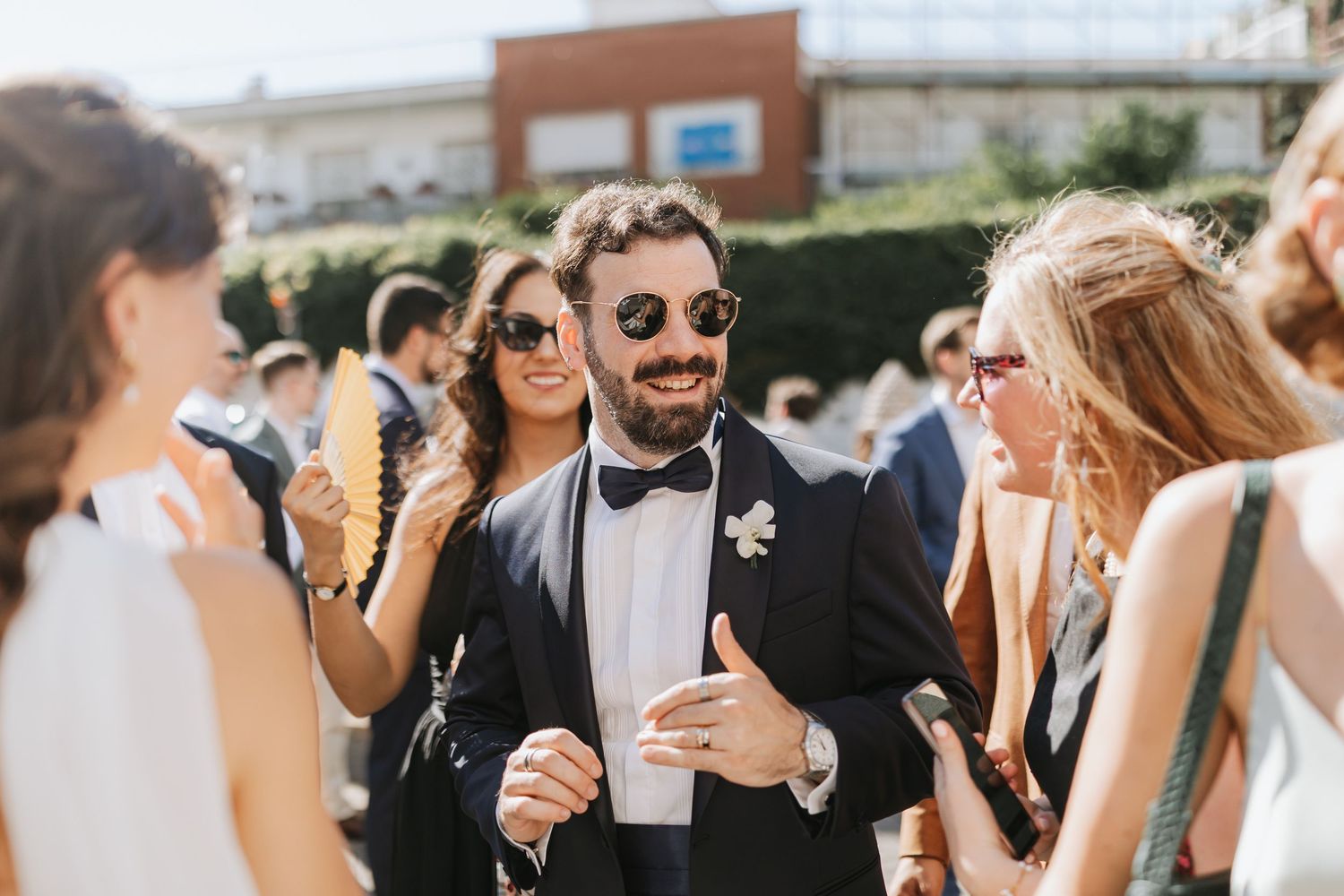 Wedding guests enjoying drinks and conversation at an outdoor reception on a sunny day.