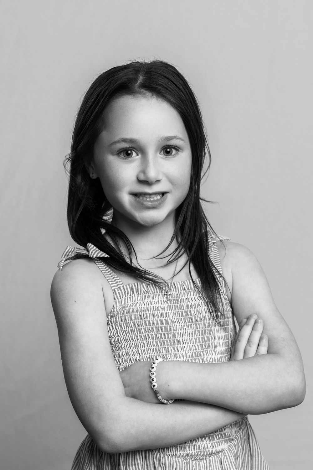 Black and white portrait of a young girl with crossed arms, smiling confidently in a sleeveless dress.