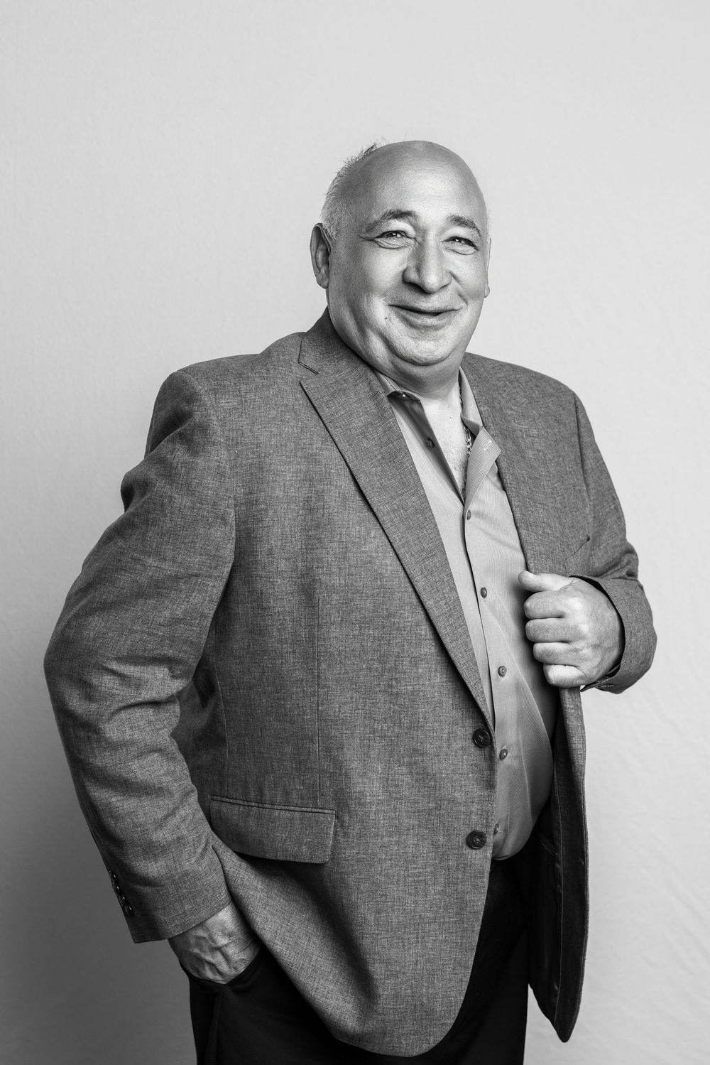 Black and white portrait of a smiling middle-aged man in a blazer, posing confidently against a light background.