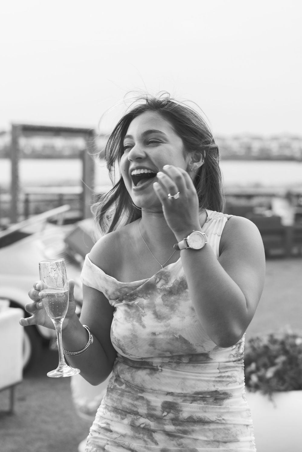 Black and white photo of a laughing woman holding a champagne glass at an outdoor rooftop event.