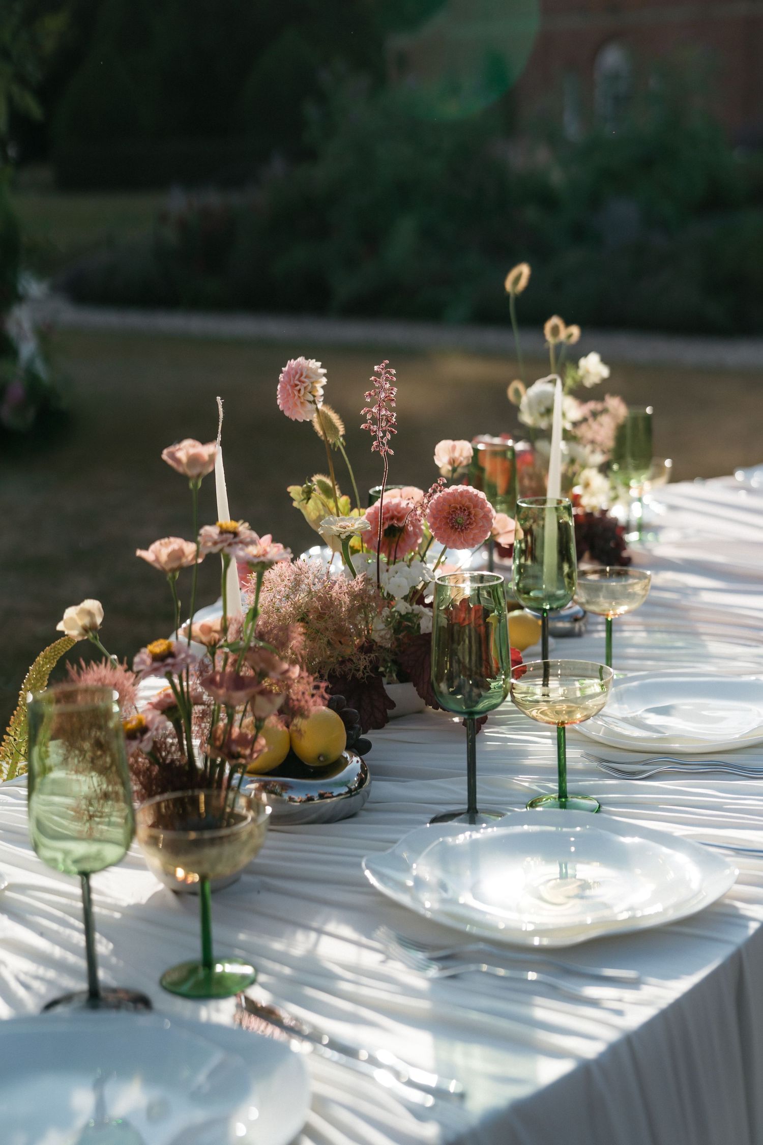 A series of elegant floral centerpieces with pink and cream blooms arranged in glass vases on a white tablecloth.