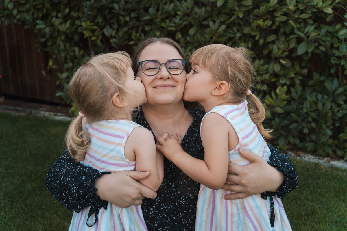 kids giving mom affectionate kisses on her cheek during their family photoshoot on a sunny day in their backyard in Rouse hill