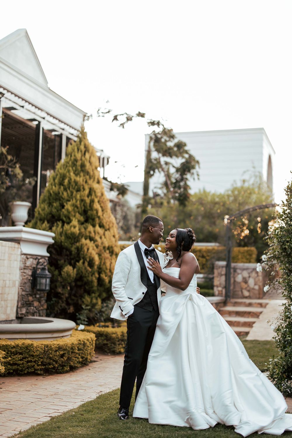 Romantic wedding couple shares intimate moments on a stone patio surrounded by lush greenery at sunset.