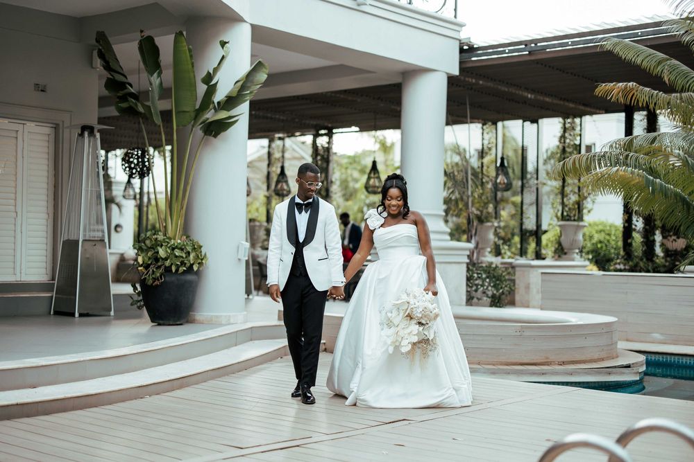 A wedding party walks through an elegant hotel lobby with white marble floors and modern glass walls.