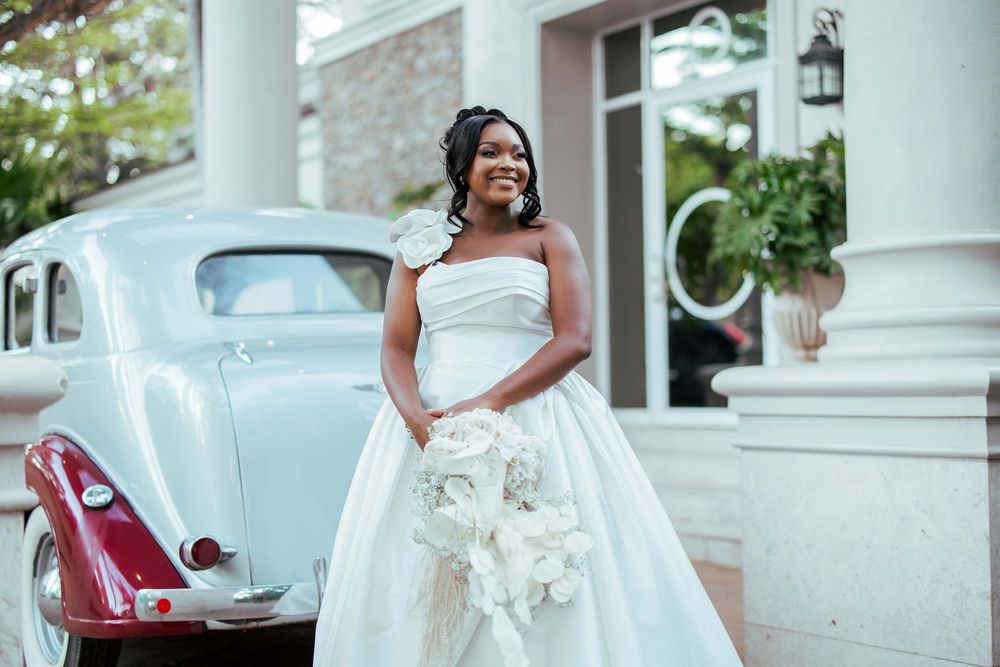 Beautiful wedding scene with a white gown and classic vintage car in front of an elegant columned entrance.