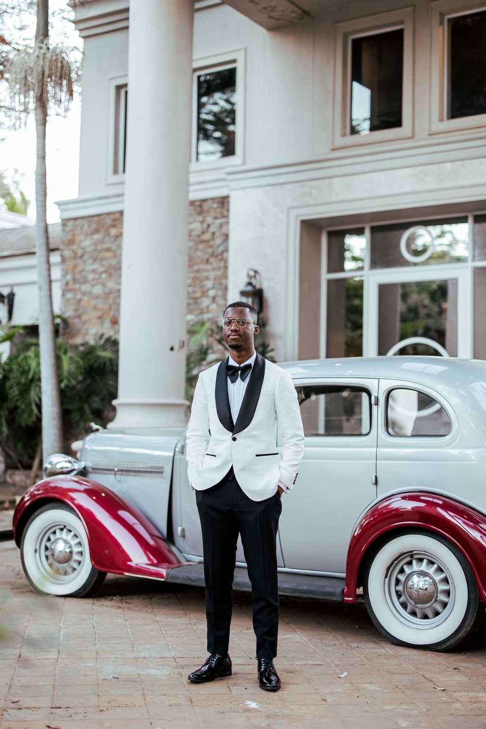 Classic vintage cars in red and silver parked outside an elegant stone mansion with white columns.