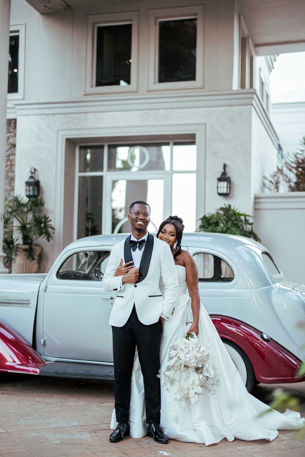 A wedding couple poses elegantly in front of a vintage car collection at Siyekahaya Estate.
