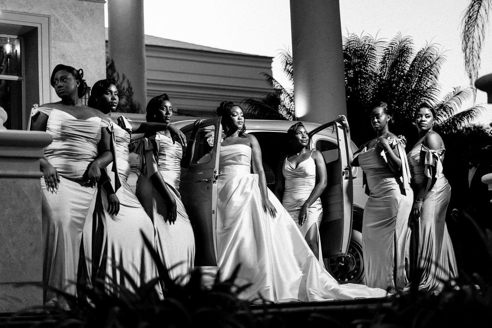 Wedding party in formal attire poses together on a porch in black and white photography.
