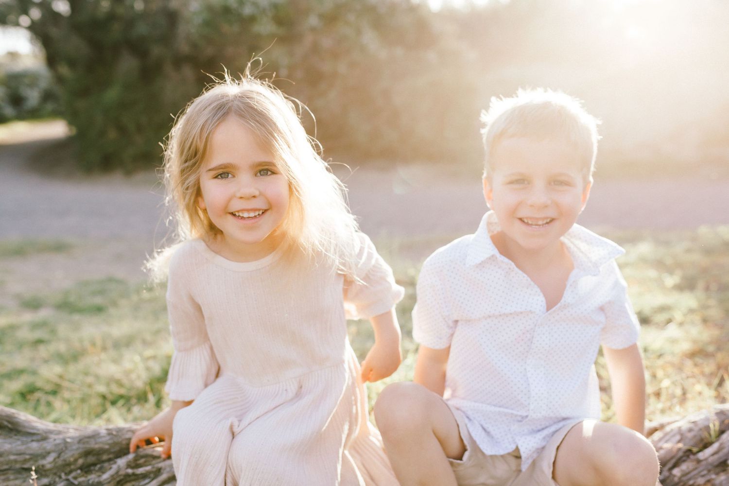 Two young children sitting outdoors laughing and playing together in warm sunlight.