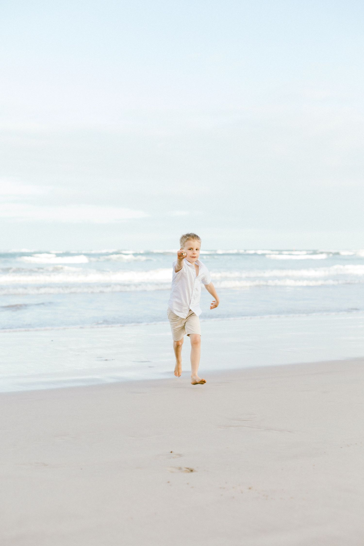 A child runs and plays along a serene beach shoreline on a bright, misty morning.