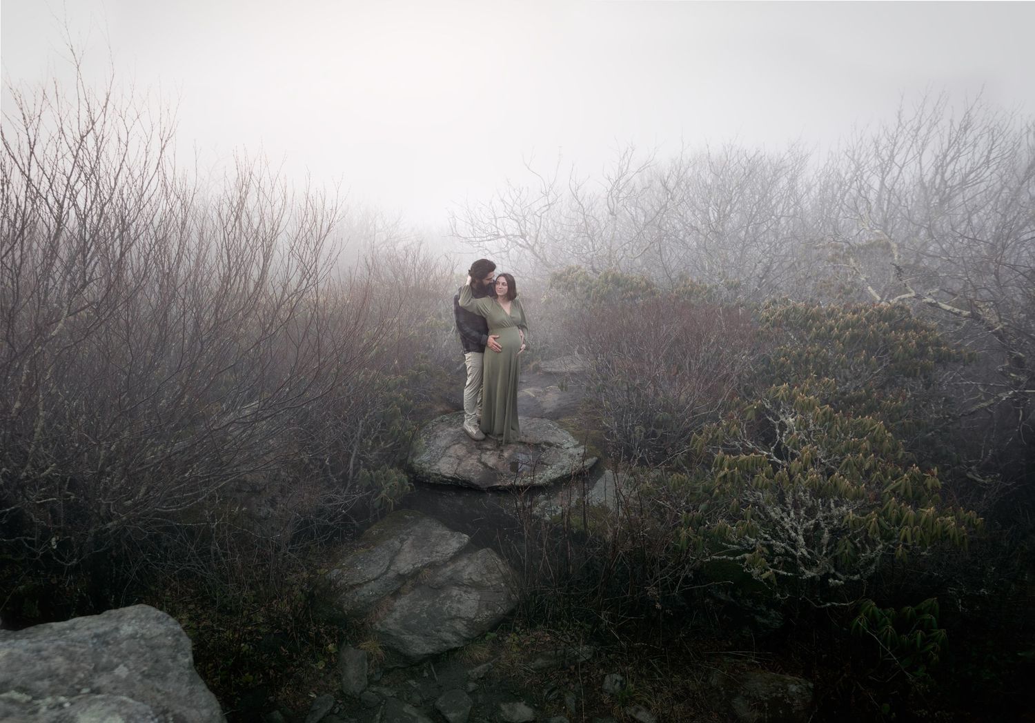 A silhouetted figure stands on a misty mountain ledge overlooking a foggy valley landscape at dawn.