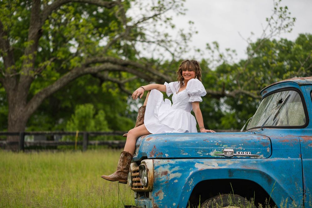 A rustic vintage blue truck parked in a grassy field with trees in the background.