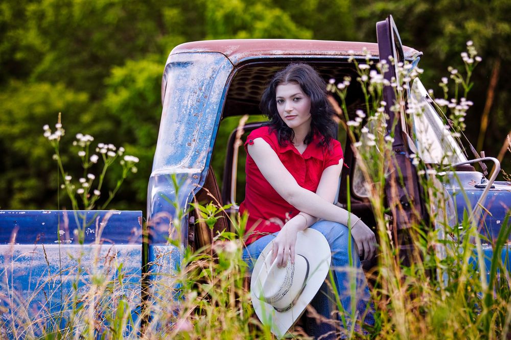 A woman in a red dress plays banjo while sitting in a wildflower meadow during golden hour.
