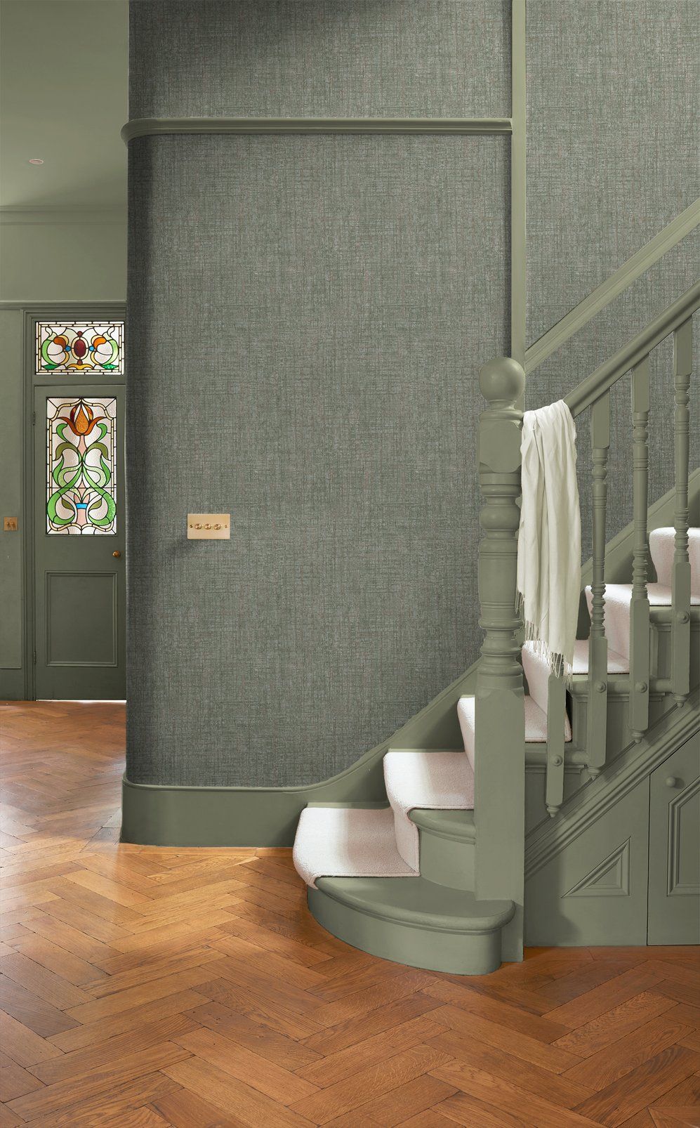 Green staircase with stained glass window panels and herringbone wood flooring in an elegant entryway. Graham & brown Armando sage wallpaper