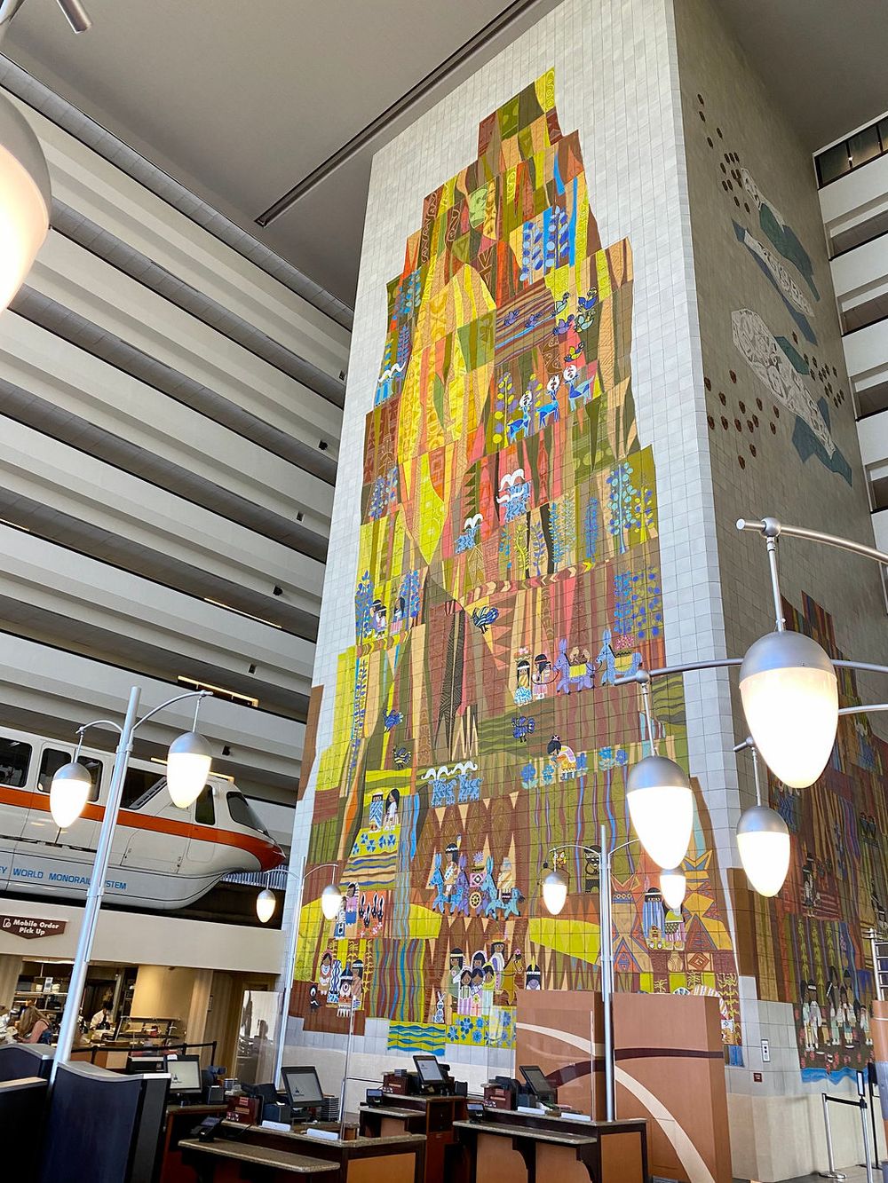 Large colorful mural artwork displayed on white walls of dining area with pendant lighting.
