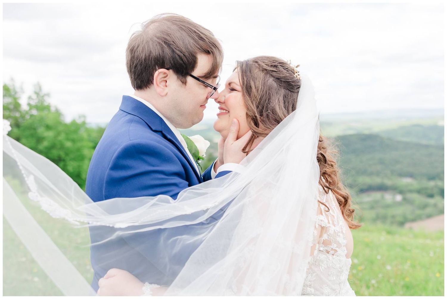 Romantic wedding moment captured with flowing veil against mountain landscape.