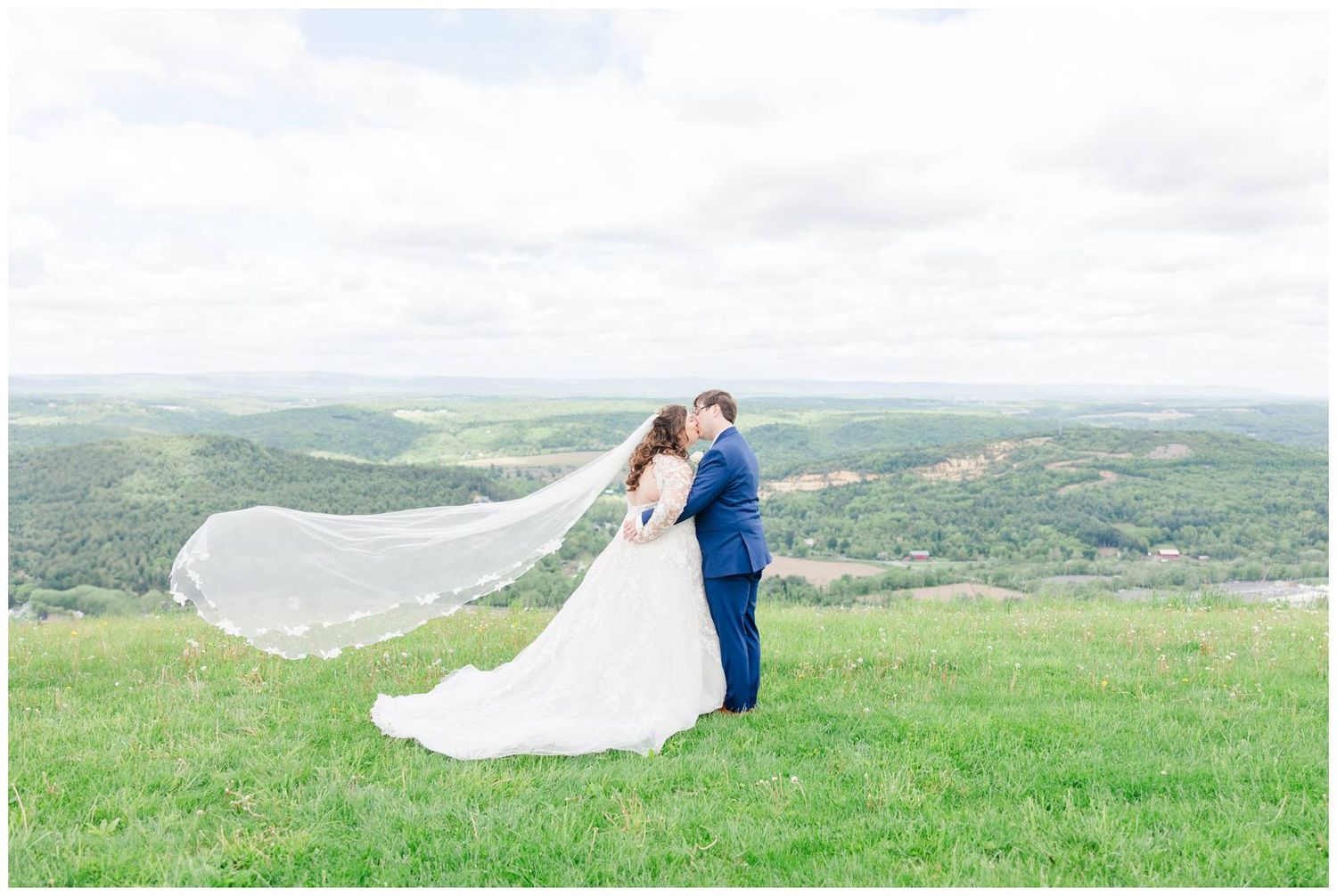 A windswept wedding moment captured on a scenic hilltop with the couple's veil flowing in the breeze.